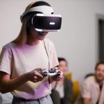 Smiling woman wearing VR headset and holding a gaming controller indoors with friends.